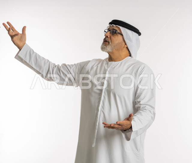 ايماءات القاء الشعر ,بورتريه لرجل كبير السن عربي خليجي اماراتي يرتدي الكندورة و الغترة و النظارت الطبية يفتح ذراعيه بتعابير الاندماج, النظر الى الاعلى بحركات تدل على التكلم مع شخص ما, خلفية بيضاء