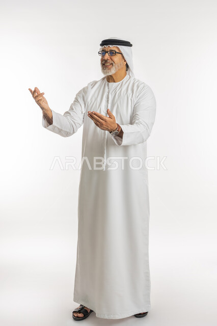ايماءات السعادة والفرح عند رؤية شخص ما, حركات تدل على الاستقبال و الترحيب, الاشارة الى شيء ما, بورتريه لرجل مسن عربي اماراتي خليجي يرتدي الكندورة و الغترة يرفع ذراعيه للاعلى بتعابير الفرح, صورة الجسم بالطول الكامل, خلفية بيضاء