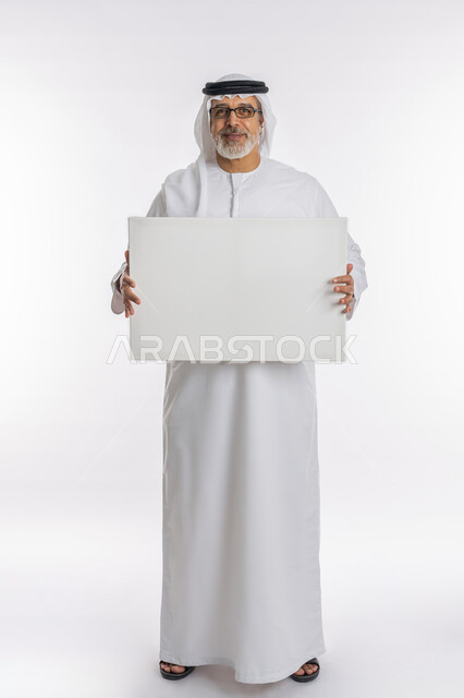تعابير الإعجاب والسرور والنظر إلى الكاميرا ،موك اب مستطيل أبيض، بورتريه لرجل مسن عربي اماراتي خليجي يرتدي الكندورة و الغترة يحمل بيديه لوحه بيضاء مستطيلة، لوح إعلاني فارغ، الوقوف باستقامه وثقه، صورة الجسم بالطول الكامل، خلفية بيضاء