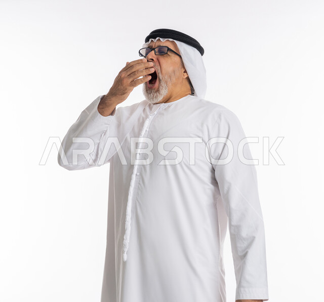 الشعور بالتعب والتثاؤب و الكسل والخمول، الإحساس بالإرهاق و الحاجه الى النوم والراحه ,بورتريه مقرب لرجل كبير السن عربي خليجي اماراتي يرتدي الكندورة والغترة والنظارات الطبية يضع يده على فمه بإيماءات تدل على النعاس, خلفية بيضاء