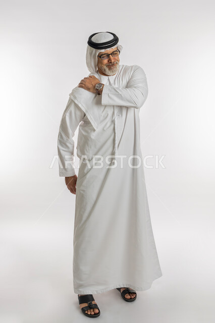 الحاجه لوضع خطة علاجية, إيماءات الألم في الأكتاف، التهاب العضلات والمفاصل، الإحساس بالتعب والإرهاق, بورتريه لرجل مسن عربي اماراتي خليجي يرتدي الكندورة و الغترة يضع يده على رقبته بتعابير الوجع، طلب المساعده للذهاب الى المستشفى، صورة الجسم بالكامل، خلفية بيضاء