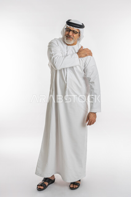 إيماءات الألم في الأكتاف، التهاب العضلات والمفاصل، الإحساس بالتعب والإرهاق, بورتريه لرجل مسن عربي اماراتي خليجي يرتدي الكندورة و الغترة يضع يده على رقبته بتعابير الوجع، الحاجه لوضع خطة علاجية, طلب المساعده للذهاب الى المستشفى، صورة الجسم بالكامل، خلفية بيضاء