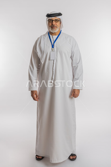 الوقوف باستقامة والنظر إلى الكاميرا، موك اب ابيض، كرت فارغ مستطيل الشكل, توضيح أهمية الهوية الشخصية، بورتريه لرجل مسن عربي اماراتي خليجي مبتسم يرتدي الغترة و الكندورة و النظارات الطبية يضع على رقبته بادج شخصي, الطول الكامل للجسم, خلفية بيضاء