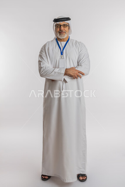 موك اب ابيض، كرت فارغ مستطيل الشكل، رجل أعمال يضع على رقبته بادج شخصي, توضيح أهمية الهوية الشخصية، بورتريه لرجل مسن عربي اماراتي خليجي مبتسم يرتدي الغترة و الكندورة و النظارات الطبية ينظر إلى الكاميرا بإيماءات أيدي متقاطعة، الطول الكامل للجسم, خلفية بيضاء