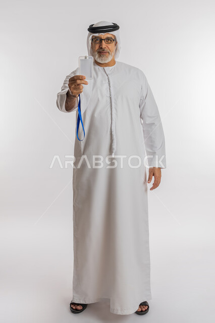 توضيح أهمية الهوية الشخصية، موك اب ابيض، عرض كرت فارغ مستطيل الشكل، بورتريه لرجل كبير السن عربي اماراتي خليجي مبتسم يرتدي الغترة و الكندورة و النظارات الطبيه يحمل بيده بطاقة تعريفية، النظر إلى الكاميرا بإيماءات السعادة والسرور، الجسم بالطول الكامل, خلفية بيضاء