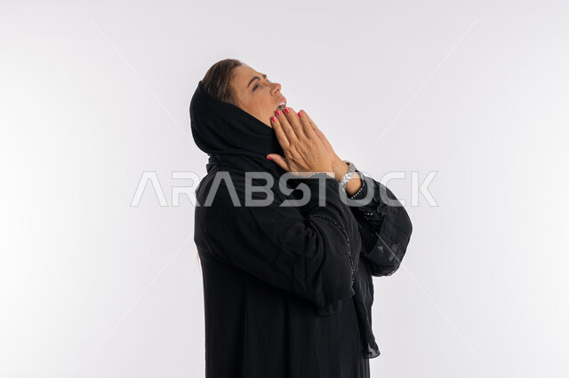 النداء لشخص ما, الحمد والشكر لله، بورتريه مقرب من الجانب لامرأة عربية سعودية محجبة ترتدي العباءة السوداء ترفع رأسها عاليا بايماءات الدعاء والتضرع، مفهوم طلب العون و المغفرة، سيدة اماراتية خليجية ترغب في تحقيق الأمنيات، خلفية بيضاء