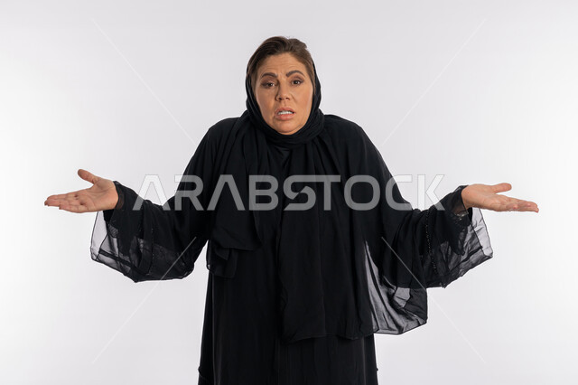الدهشة  و الصدمة و الاستغراب عند سماع خبر ما، سيدة سعودية عربية تفتح يديها بتعابير الإستفهام حول موضوع معين, الغموض وعدم الوضوح، بورتريه مقرب لامرأة خليجية اماراتية محجبة ترتدي العباءة السوداء تفتح ذراعيها بإيماءات عدم المعرفة, خلفية بيضاء