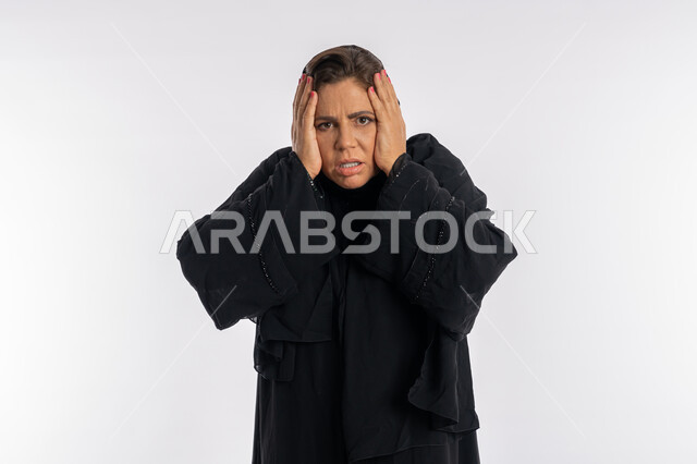 الامراض النفسيه و الحياه الفاشله, تعابير الصدمة و الدهشة,بورتريه مقرب لامرأة عربيه خليجية اماراتية محجبة ترتدي العباءة السوداء تضع يديها على وجهها بإيماءات الغضب, سيدة سعودية تشعر بالندم على فعل شي ما, الوقوع في مصيبة, خلفية بيضاء