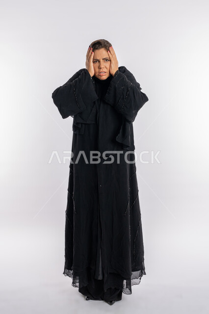 الوقوع في مصيبة, الامراض النفسيه و الحياه الفاشله, تعابير الصدمة و الدهشة,بورتريه لامرأة عربيه خليجية اماراتية محجبة ترتدي العباءة السوداء تضع يديها على وجهها بإيماءات الغضب, سيدة سعودية تشعر بالندم على فعل شي ما, الجسم بالطول الكامل, خلفية بيضاء