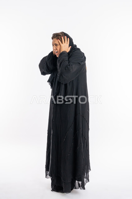 تعابير الصراخ الشديد و العصبية ,بورتريه لامرأة عربيه خليجية اماراتية محجبة ترتدي العباءة السوداء تضع يديها على رأسها بإيماءات الغضب, سيدة سعودية تشعر بالندم على فعل شي ما, الوقوع في مصيبة ,الامراض النفسيه و الحياه الفاشله ,الجسم بالطول الكامل, خلفية بيضاء