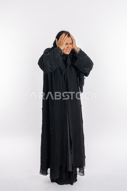 الندم على شيء ما و الشعور بالاحباط, بورتريه لإمرأة عربيه سعوديه محجبة ترتدي العباءه السوداء تضع يديها على رأسها بتعابير الدهشه و الانزعاج, الوقوع في مصيبه, سيدة اماراتية خليجية تشعر بالخسارة و الحزن, الجسم بالطول الكامل, خلفية بيضاء