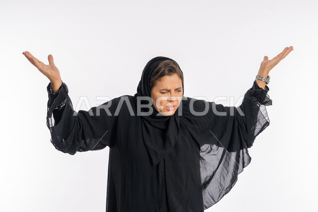 فتح الذراعين بإيماءات الانفعال الشديد، بورتريه مقرب لامرأه عربيه خليجيه سعودية محجبة ترتدي العباءة السوداء ترفع اليدين بتعابير العصبية و الصراخ والغضب، سيدة اماراتية تشعر بالإنزعاج والقهر، خلفية بيضاء