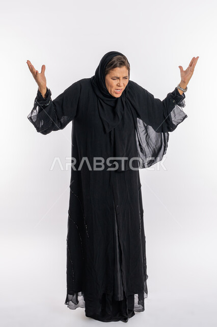 حركات تدل على الحزن و الخسارة والعصبية, فتح الذراعين بإيماءات الانفعال الشديد، بورتريه لامرأه عربيه خليجيه سعودية محجبة ترتدي العباءة السوداء ترفع اليدين بتعابير الصراخ والغضب، سيدة اماراتية تشعر بالإنزعاج والقهر، صورة الجسم بالطول الكامل, خلفية بيضاء