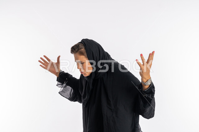 رفع اليدين بتعابير الصراخ والغضب، بورتريه مقرب لامرأه عربيه خليجيه سعودية محجبة ترتدي العباءة السوداء تفتح ذراعيها  بإيماءات الانفعال الشديد، سيدة اماراتية تشعر بالإنزعاج والقهر، خلفية بيضاء