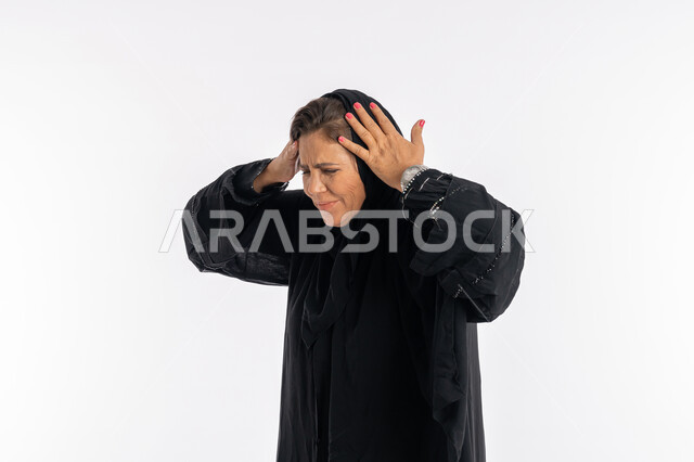 الوقوع في مصيبه, الشعور بالاحباط و الندم على شيء ما, بورتريه مقرب لإمرأه عربيه سعوديه محجبة ترتدي العباءه السوداء تضع يديها على رأسها بتعابير الدهشه و الانزعاج, سيدة اماراتية خليجية تشعر بالخسارة و الحزن, خلفية بيضاء