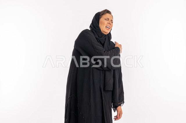 التهاب المفاصل و الاعصاب و العضلات، الحاجه للعلاج وطلب المساعده، بورتريه لامرأة خليجيه إماراتية ترتدي العباءة السوداء تشعر بالمرض و التعب، سيدة عربية سعودية تضع يدها على كتفها بإيماءات تدل على الألم الشديد، خلفية بيضاء