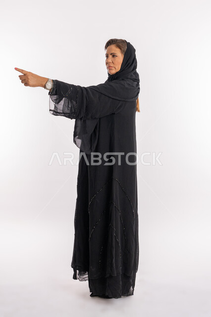 إلقاء اللوم و الاتهام، طلب التوقف عن فعل الأخطاء، امرأة خليجية اماراتية تشعر بالإنزعاج والرغبة بالإنتقام، بورتريه مقرب من الجانب لسيدة عربية سعودية ترتدي العباءة السوداء ترفع اصبع السبابه لتحديد شخص ما ( أنت )، الجسم بالطول الكامل, خلفية بيضاء