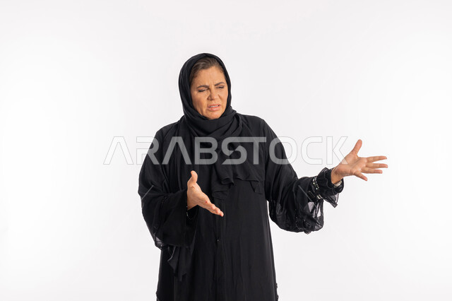 النظر الى شيء ما بتعابير الاشمئزاز ,بورتريه مقرب لسيدة عربيه سعودية محجبة ترتدي العباءة السوداء تفتح ذراعيها بايماءات النفور, امرأة اماراتية خليجية ترفع يديها بحركات تدل على القرف, خلفية بيضاء