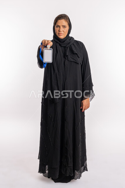 توضيح أهمية الهوية الشخصية، موك اب ابيض، عرض كرت فارغ مستطيل الشكل، بورتريه لامرأة عربية سعودية مبتسمة ترتدي العباءة السوداء تحمل بيدها بطاقة تعريفية، سيدة خليجية إماراتية تنظر إلى الكاميرا بإيماءات الثقة بالنفس، الجسم بالطول الكامل, خلفية بيضاء