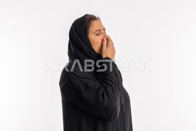 السهر لوقت متأخر, النعاس والارهاق والحاجة إلى النوم, امراه سعودية تشعر بالكسل والخمول وطلب الراحة, بورتريه مقرب من الجانب لسيدة عربيه خليجية اماراتية محجبة ترتدي العباءة السوداء تضع يدها على فمها تقوم بالتثاؤب, خلفية بيضاء