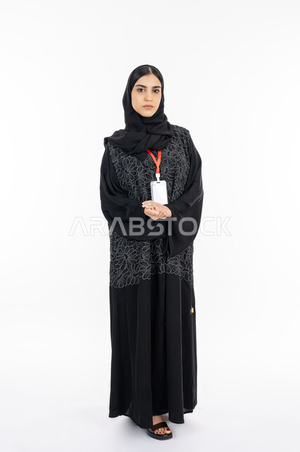 موك أب أبيض مفرغ, الوقوف باستقامة بإيماءات الجدية والثقة بالنفس, بورتريه لإمرأة عربية خليجية إماراتية ترتدي العباءة تضع بادج شخصي بشريط أحمر, سيدة سعودية تنظر إلى الكاميرا, أناقة النساء الخليجيات, الاهتمام بالمظهر الخارجي, صورة الجسم بالطول الكامل, خلفية بيضاء