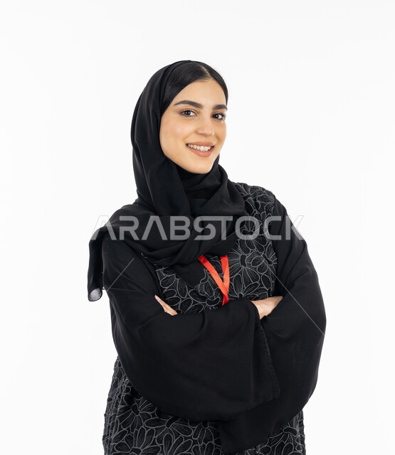 The concept of femininity and concern for external appearance, the elegance of Gulf women, a portrait of an Arab Gulf Emirati young woman wearing an abaya, standing with crossed hand gestures, a smiling Saudi woman looking at the camera confidently, white background
