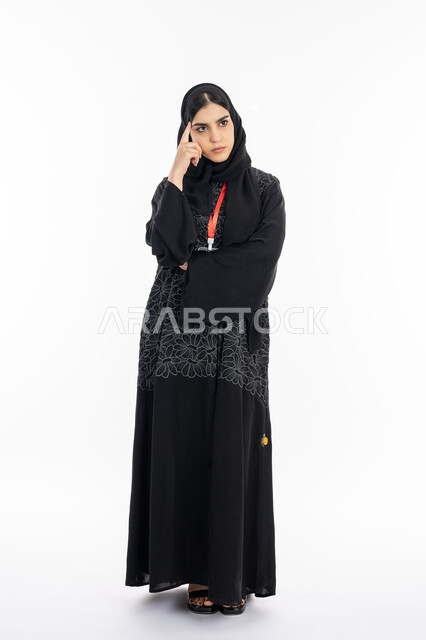 التفكير والحيرة وصعوبة اختيار شيء ما, ايجاد حل لمشكلة معينة, شرود الذهن والتخطيط لشيء معين, بورتريه لشابة عربية خليجية إماراتية ترتدي العباءة تقف بتعابير السؤال, سيدة سعودية تضع يديها على وجهها, صورة الجسم بالطول الكامل, خلفية بيضاء