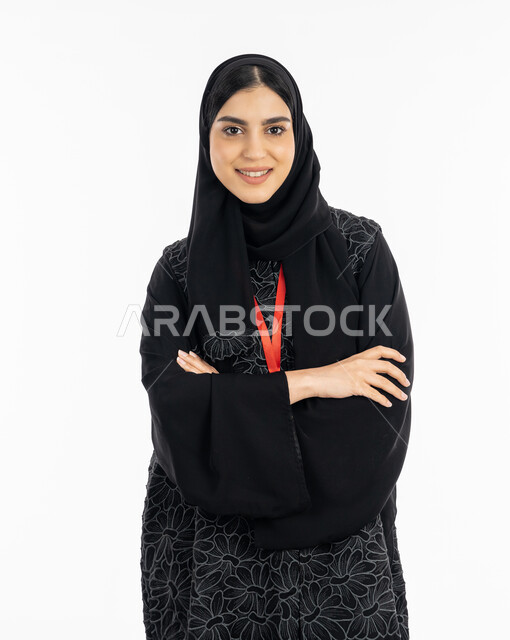 أناقة النساء الخليجيات, الاهتمام بالمظهر الخارجي,  بورتريه لشابة عربية خليجية إماراتية ترتدي العباءة تقف بإيماءات ايدي متقاطعة, سيدة سعودية مبتسمة تنظر إلى الكاميرا بثقة, خلفية بيضاء