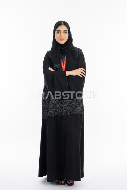 الاهتمام بالمظهر الخارجي, أناقة النساء الخليجيات, بورتريه لشابة عربية خليجية إماراتية ترتدي العباءة تقف بإيماءات ايدي متقاطعة, سيدة سعودية تنظر إلى شيء ما بثقة, صورة الجسم بالطول الكامل, خلفية بيضاء