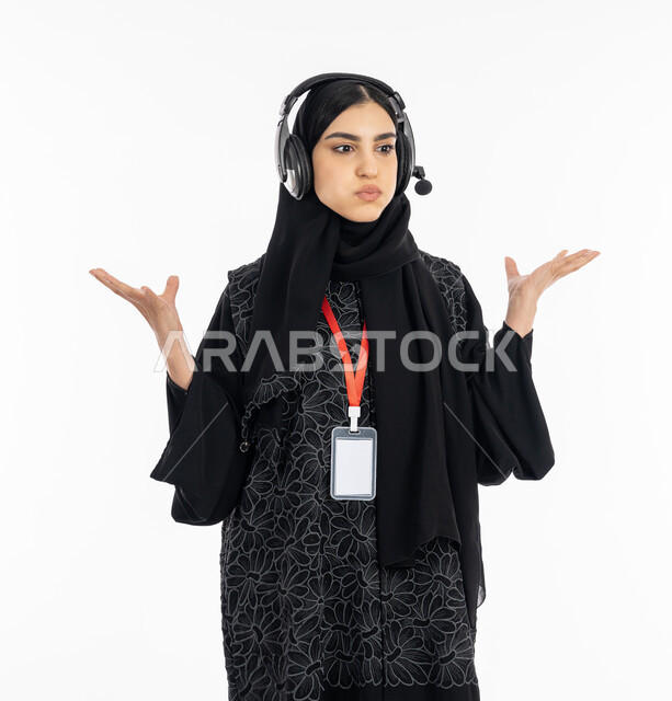 الوقوف بإيماءات الغضب من شيء ما, رفع اليدين للأعلى بانزعاج وعدم تقبل أمر معين, بورتريه لشابة عربية خليجية إماراتية ترتدي العباءة تعمل في مجال خدمة العملاء, سيدة سعودية تقوم بالرد على اسئلة الزبائن, ارتداء بطاقة تعريفية مستطيلة فارغة, خلفية بيضاء