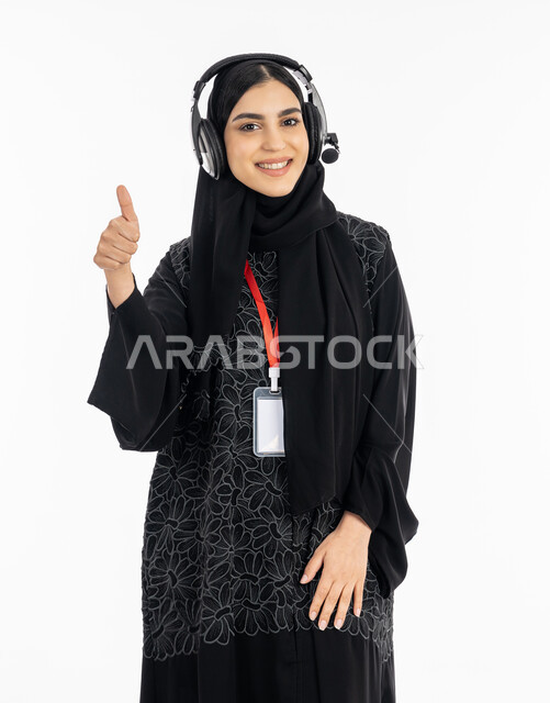 Integrating work with technology and technology in practical life, a Saudi woman looking at the camera, responding to customer questions and inquiries in the technical support department, a portrait of a smiling Arab Gulf Emirati woman wearing an abaya, raising her finger with the sign of quality and excellence, white background