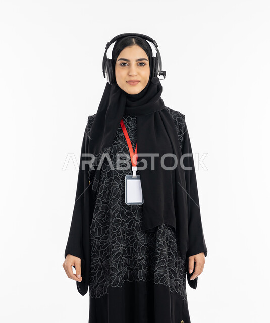 An empty rectangular white mockup, standing straight and looking at the camera, a portrait of an Arab Gulf Emirati woman wearing an abaya using headphone technology, a Saudi woman working in the field of customer service and answering customer inquiries, presenting radio programs, white background
