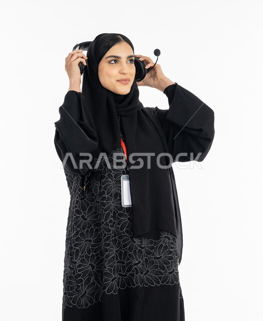 الرد على استفسارات الزبائن ببشاشة، ارتداء بادج شخصي بشريط أحمر, تقديم البرامج الاذاعية، بورتريه لإمرأة عربية خليجية اماراتية ترتدي العباءة تضع سماعة الهيدفون، الاندماج والنظر إلى شيء ما بسرور, سيدة سعودية تعمل في مجال خدمة العملاء, خلفية بيضاء