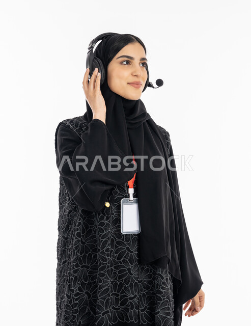 تقديم البرامج الاذاعية، بورتريه لإمرأة عربية خليجية اماراتية ترتدي العباءة تضع سماعة الهيدفون، العمل في مجال خدمة العملاء، الاندماج والنظر إلى شيء ما بسرور, سيدة سعودية تقوم بالرد على استفسارات الزبائن ببشاشة، ارتداء بادج شخصي بشريط أحمر, خلفية بيضاء