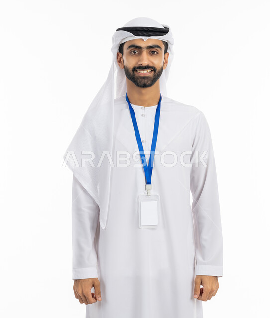 النظر إلى الكاميرا بتعابير البهجة والفرح, الاهتمام بالمظهر الخارجي والأناقة الاماراتية, موك اب بطاقة تعريفية مفرغة باللون الابيض، بورتريه لرجل عربي خليجي إماراتي يرتدي الكندورة والغترة يقف بابتسامة, ارتداء بادج شخصي, خلفية بيضاء