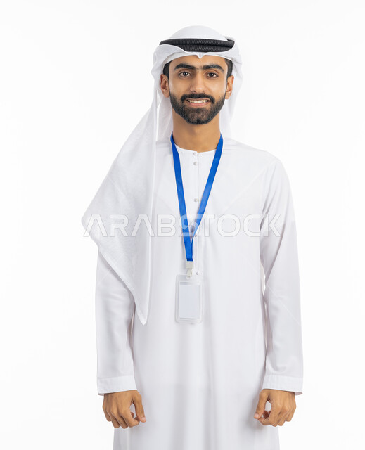 الرجولة والاهتمام بالمظهر الخارجي, النظر إلى الكاميرا بتعابير البهجة والفرح، موك اب بطاقة تعريفية مفرغة باللون الابيض, بورتريه لرجل عربي خليجي إماراتي يرتدي الكندورة والغترة الاماراتية يقف بابتسامة, ارتداء بادج شخصي, خلفية بيضاء
