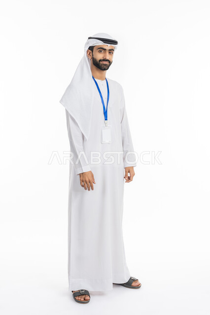 الاهتمام بالمظهر الخارجي, مفهوم الوسامة والرجولة, كرت أبيض مستطيل فارغ, ارتداء بادج شخصي, بورتريه لرجل عربي خليجي إماراتي مبتسم يرتدي الكندورة والغترة ينظر إلى الكاميرا ويضع بطاقة شخصية تعريفية بشريط أزرق, صورة الجسم بالطول الكامل, خلفية بيضاء