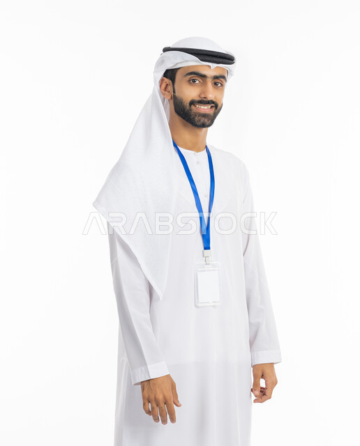 A blank rectangular white card, wearing a personal badge, the concept of elegance, masculinity, and concern for external appearance, a portrait of a smiling Arab Gulf Emirati man wearing a kandora and ghutra, looking at the camera and wearing an identification card with a blue ribbon, white background.