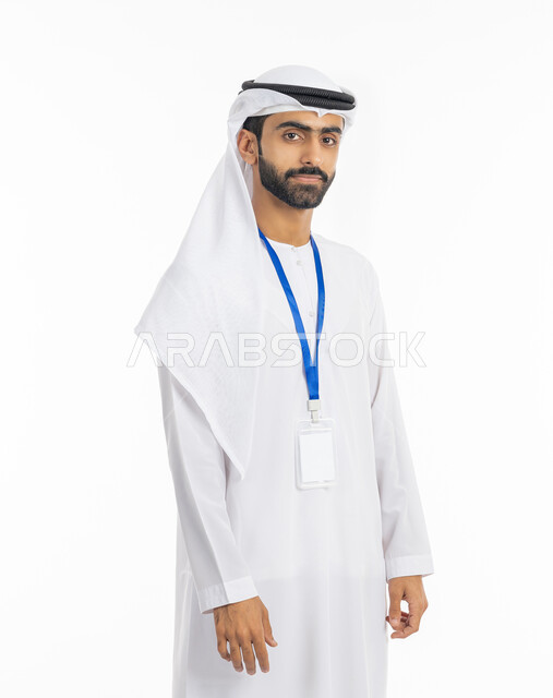 ارتداء بادج شخصي, النظر إلى الكاميرا بتعابير الجدية, كرت أبيض مستطيل فارغ, مفهوم الأناقة والرجولة والاهتمام بالمظهر الخارجي, بورتريه لرجل عربي خليجي إماراتي يرتدي الكندورة والغترة يضع بطاقة شخصية تعريفية بشريط أزرق, خلفية بيضاء