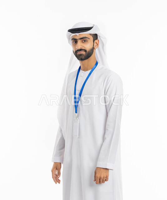 The concept of handsomeness and masculinity, attention to external appearance, a portrait of an Emirati Gulf Arab man wearing the Emirati kandora and ghutra, looking at the camera, standing confidently and wearing a personal badge, personal identification card with the employee’s name, white background