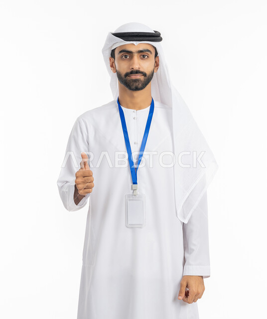 رفع الإصبع بإيماءات الجودة والامتياز, بورتريه لرجل أعمال عربي خليجي إماراتي يرتدي الكندورة والغترة ينظر إلى الكاميرا بابتسامة, ارتداء بادج شخصي, بطاقة تعريفية شخصية باسم الموظف, موك أب أبيض مستطيل فارغ, خلفية بيضاء