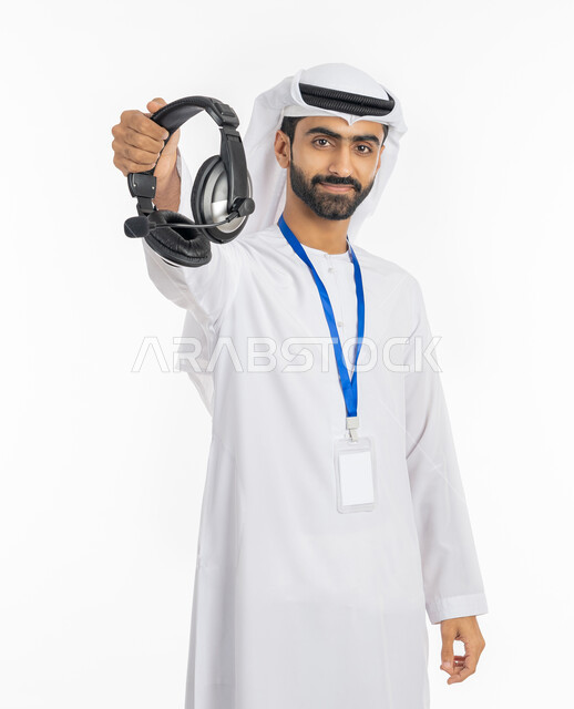 مفهوم خدمة العملاء, استخدام تقنية الهيدفون, العمل في مجال التوزيع الموسيقي, تقديم البرامج الاذاعية,  بورتريه لرجل عربي خليجي إماراتي مبتسم يرتدي الكندورة والغترة يضع بطاقة تعريفية شخصية للموظفين ويعرض سماعة الرأس, خلفية بيضاء