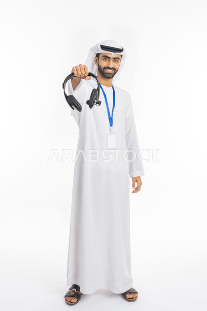 العمل في مجال التوزيع الموسيقي, تقديم البرامج الاذاعية, مفهوم خدمة العملاء, بورتريه لرجل عربي خليجي إماراتي مبتسم يرتدي الكندورة والغترة يضع بطاقة تعريفية شخصية للموظفين ويعرض سماعة الرأس, استخدام تقنية الهيدفون, صورة الجسم بالطول الكامل, خلفية بيضاء