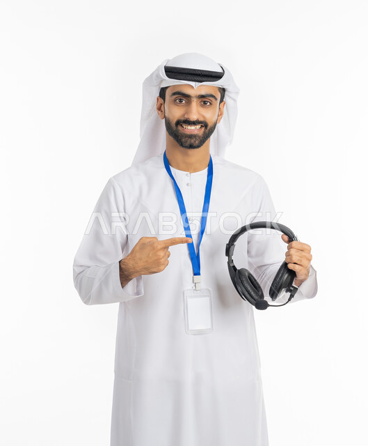 الرد على اسئلة الزبائن, العمل في مجال خدمة العملاء, تقديم البرامج الاذاعية, بورتريه لشاب عربي خليجي إماراتي يرتدي الكندورة والغترة الاماراتية يشير بإصبعه إلى سماعة الرأس, استخدام تقنية الهيدفون, بطاقة شخصية تعريفية بشريط أزرق, خلفية بيضاء