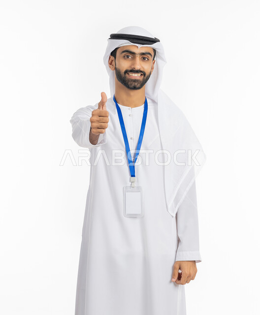 رفع الإصبع بإيماءات الجودة والامتياز, بورتريه لرجل عربي خليجي إماراتي يرتدي الكندورة والغترة ينظر إلى الكاميرا بابتسامة, ارتداء بادج شخصي, بطاقة تعريفية شخصية باسم الموظف, موك أب أبيض مستطيل فارغ, خلفية بيضاء