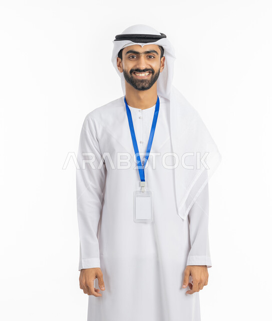 ارتداء بادج شخصي, أناقة الشباب في الامارات, مفهوم الرجولة والاهتمام بالمظهر الخارجي, النظر إلى الكاميرا بتعابير البهجة والفرح, موك اب بطاقة تعريفية مفرغة باللون الابيض، بورتريه لرجل عربي خليجي إماراتي يرتدي الكندورة والغترة الاماراتية يقف بابتسامة, خلفية بيضاء