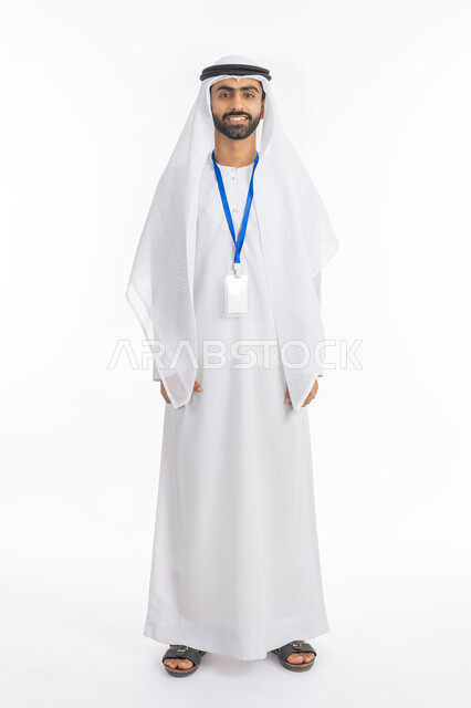 موك اب بطاقة تعريفية مفرغة باللون الابيض, مفهوم الرجولة والاهتمام بالمظهر الخارجي, النظر إلى الكاميرا بتعابير البهجة والفرح، بورتريه لرجل عربي خليجي إماراتي يرتدي الكندورة والغترة الاماراتية يقف بابتسامة, ارتداء بادج شخصي, صورة الجسم بالطول الكامل, خلفية بيضاء