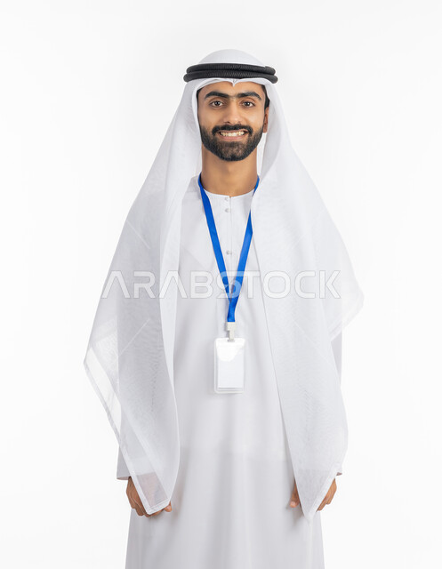 أناقة الشباب في الامارات, مفهوم الرجولة والاهتمام بالمظهر الخارجي, النظر إلى الكاميرا بتعابير البهجة والفرح, موك اب بطاقة تعريفية مفرغة باللون الابيض، بورتريه لرجل عربي خليجي إماراتي يرتدي الكندورة والغترة الاماراتية يقف بابتسامة, ارتداء بادج شخصي, خلفية بيضاء