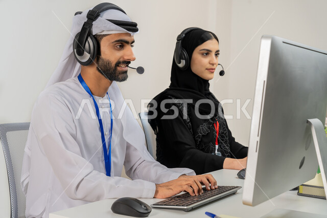 مساهمة النساء في الوظائف المكتبية، دمج التقنيات الحديثة والمتطورة في الحياة العملية، بورتريه مقرب لموظفين عربيين خليجيين اماراتيين يجلسان في المكتب يقومان بالتعاون والتشارك في اداء المهام، استخدام تقنية الهيدفون بالرد على استفسارات العملاء, خلفية رمادية