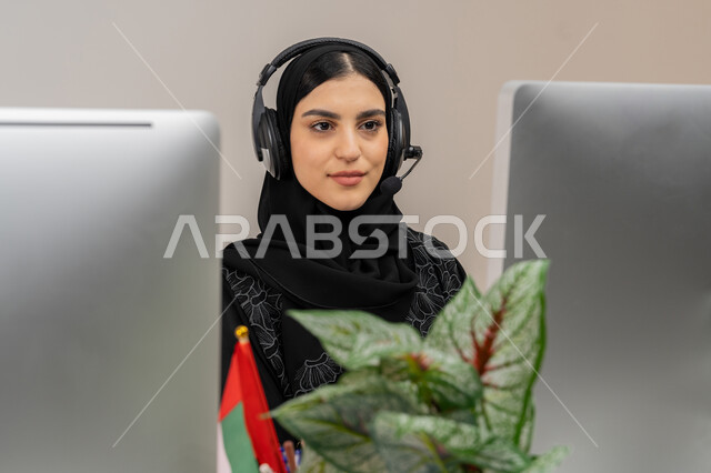دمج التقنيات الحديثة والمتطورة في الحياة العملية, تحضير وتقديم البرامج الإذاعية، إمرأة سعودية تعمل في مجال خدمة الزبائن، الإجابة على أسئلة العملاء، بورتريه مقرب لموظفة عربية خليجية اماراتية ترتدي العباءة تقوم بأداء المهام اليومية على الحاسوب، خلفية رمادية